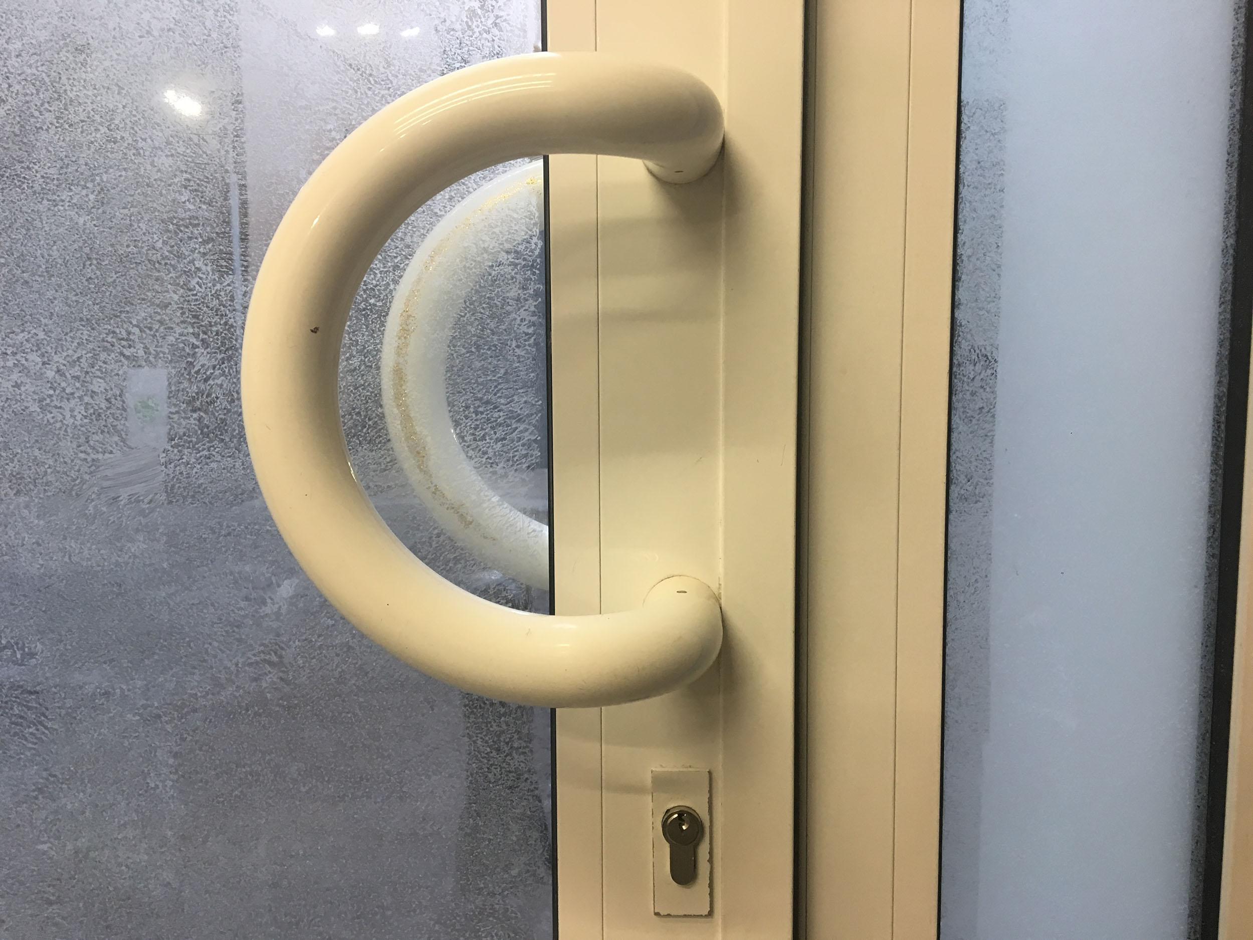 Photo d'une poignée de porte vitrée. Sur le reflet on apperçoit quelque chose derrière la poignée.